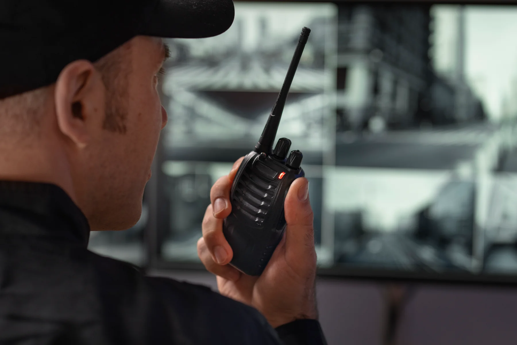 Profissional de portaria com rádio comunicador diante de telas de CFTV